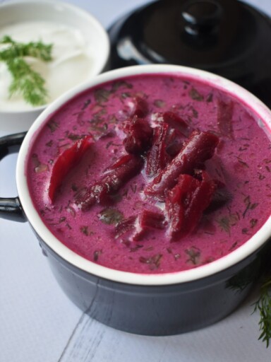 Garnuszek czerwonego barszczu, obok miseczka ze śmietaną, udekorowana koperkiem